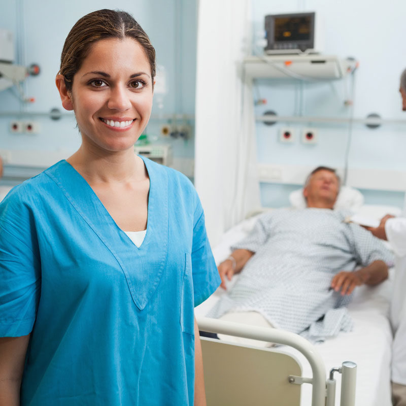 Happy nurse standing in hospital room with doctor and patient talking in background